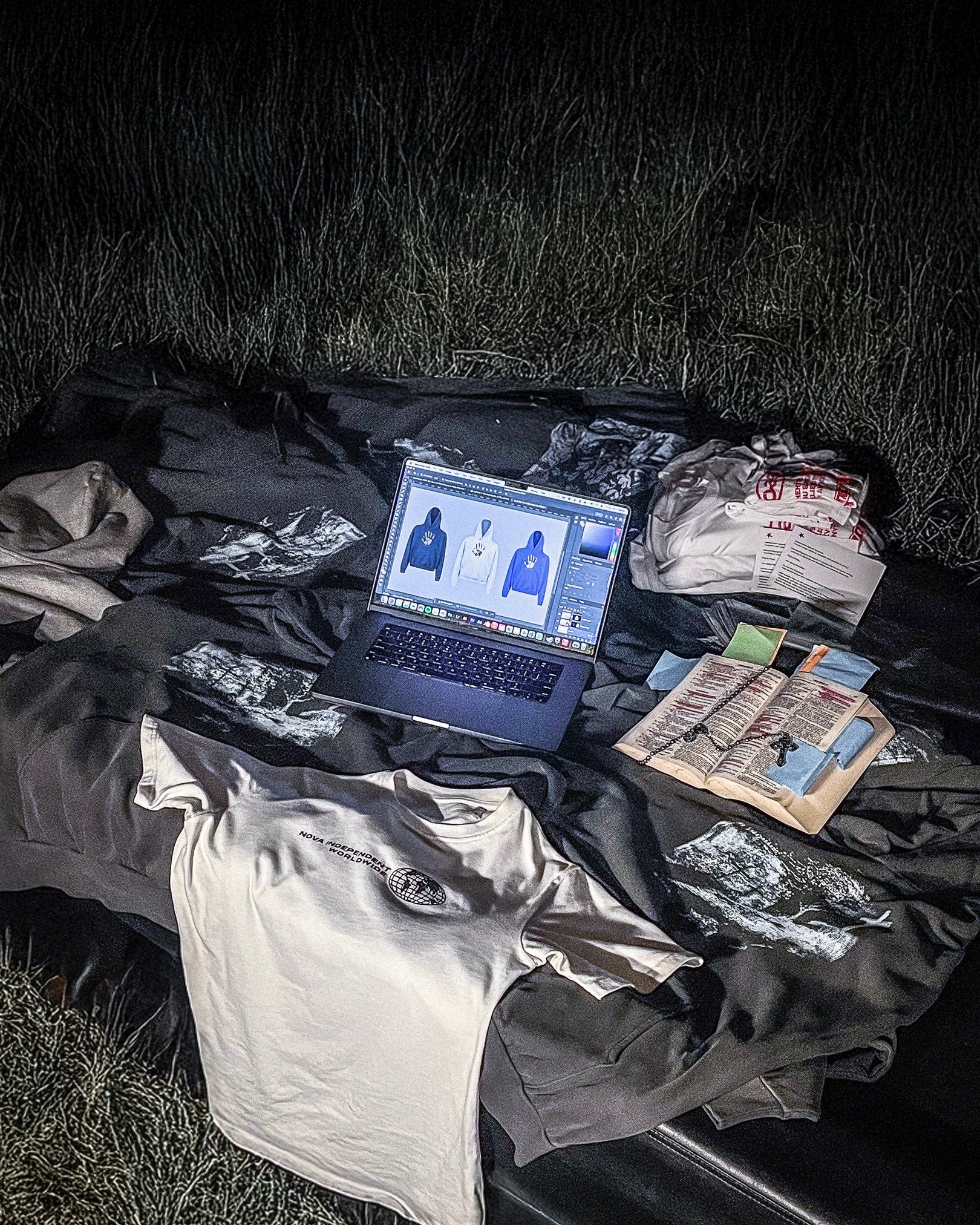 Laptop on a black blanket with clothes and documents on a grassy background